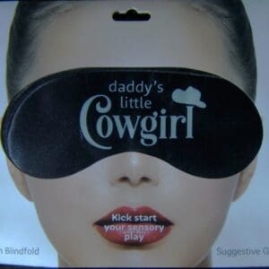 A woman wearing a black eye mask with the words " daddy 's little cowgirl " on it.