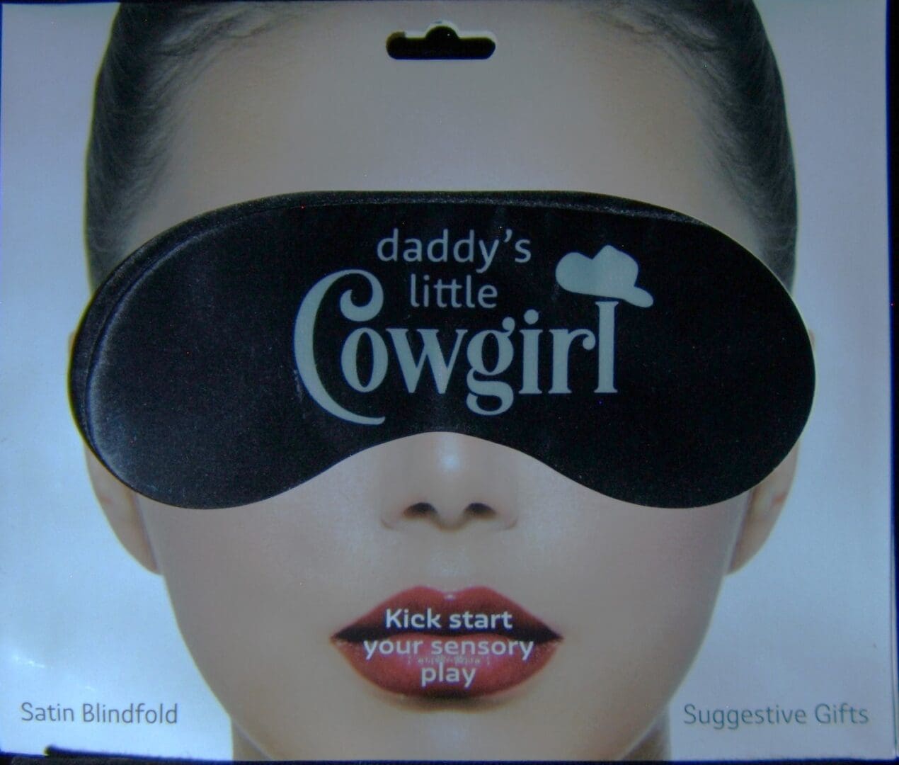 A woman wearing a black eye mask with the words " daddy 's little cowgirl " on it.